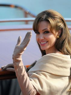 the woman is waving out her hand while standing next to a car and wearing gloves