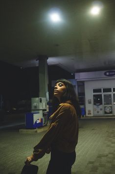 a woman standing in front of a gas station holding a suitcase and looking up at the sky