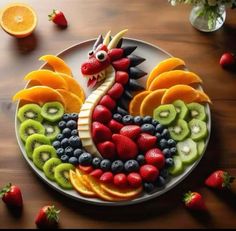 a plate that has fruit in the shape of a dragon on it and some strawberries