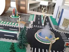 a toy model of a street with trees and buildings in the background, including a fountain