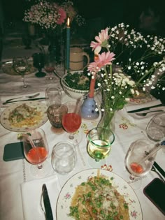 a dinner table with plates and glasses on it, flowers in vases and candles