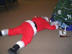 a man dressed as santa claus laying on the floor next to a small christmas tree