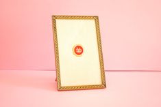 a gold frame with a red and yellow emblem on the front sits against a pink background