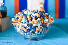 a bowl filled with blue and orange popcorn next to a cupcake on a table