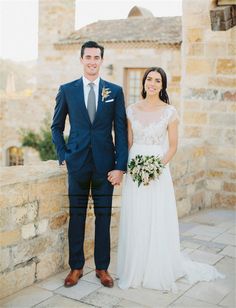 a man and woman standing next to each other in front of a stone wall holding hands