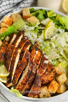 a bowl filled with chicken, lettuce and croutons next to lemon wedges