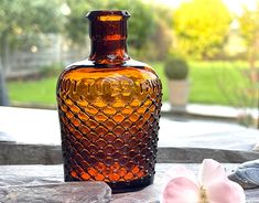 a brown glass bottle sitting on top of a table next to a flower and rocks