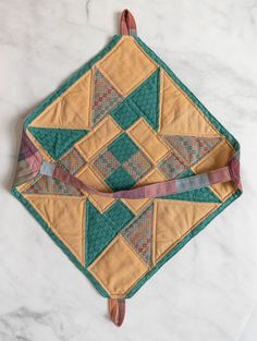 a green and yellow quilted placemat on a marble counter top with leather handles