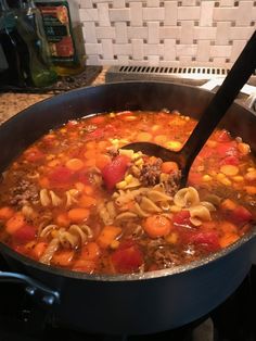 a pot filled with pasta and meat soup on top of a stove next to a wooden spoon