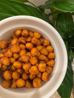 a white bowl filled with cooked chickpeas on top of a table next to green leaves