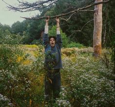 a man standing in the middle of a forest with his hands up above his head