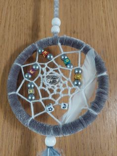 a white and gray dream catcher with beads on it's sides sitting on a wooden table