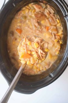 a spoon full of chicken and corn soup in a crock pot on the stove