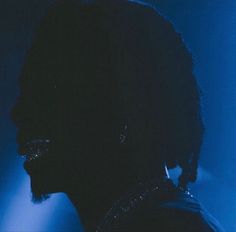 the silhouette of a man with dark hair and piercings on his ear, against a blue background