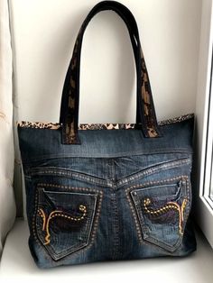 a denim purse with leopard print on the front and side pockets, hanging from a window sill