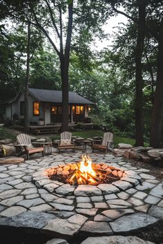 Backyard fire pit surrounded by Adirondack chairs with a cozy house tucked in the trees. Fire Pit Ground Ideas, Luxury Fire Pit Ideas Backyard, Fire Pit By Pond, Large Stone Fire Pit, Cabin Outdoor Ideas Backyards, Lake Fire Pit, River Rock Fire Pit Area, Natural Fire Pit Ideas, River Rock Fire Pit