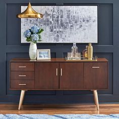 a wooden sideboard with two vases and flowers on it in front of a blue wall