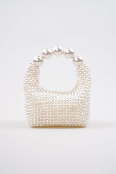 Introducing the stunning Nuit Blanche Pearl Bag by Vanina, a true embodiment of luxury and sophistication. Impossibly chic, this exquisite bag is a true masterpiece of artistry and craftsmanship that will become a wedding piece you will cherish for years to come. This bag boasts a radiant, iridescent white hue that shimmers and sparkles in the light, adding an ethereal and enchanting touch to your ensemble. Each pearl has been meticulously hand-sewn onto the bag, creating a seamless, flawless finish that exudes elegance and refinement. All of Vanina's pieces are handcrafted by skilled artisans in Lebanon, using ethically sourced and sustainable materials, making it an environmentally conscious choice you can feel good about. White All-over faux pearl embellishments Curved beaded top handle High-end White Box Bag For Gifts, Luxury White Box Bag Shaped As Clutch, Luxury Top Handle Shoulder Bag For Events, Luxury Top Handle Evening Bag For Events, Luxury Evening Bag With Top Handle For Events, Luxury White Square Evening Bag, White Luxury Rectangular Evening Bag, Luxury White Rectangular Evening Bag, Elegant White Bag With Round Handle