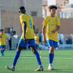 two young boys are playing soccer on the field in yellow and blue uniforms, with one boy looking at the ball