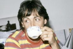 a man in striped shirt drinking from a coffee cup with his eyes wide open and looking at the camera