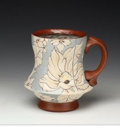 a coffee cup with a flower design on it's side and a wooden handle