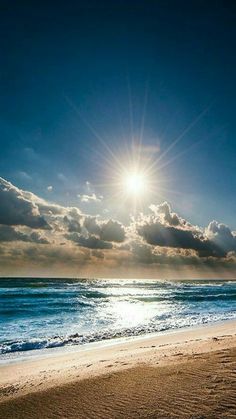 the sun shines brightly over an ocean beach with waves crashing on it and clouds in the sky