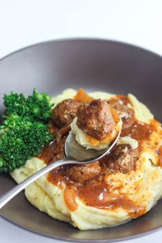 a plate with mashed potatoes, meatballs and gravy on it next to broccoli