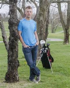 a man standing next to a golf bag in the grass near trees and a tee