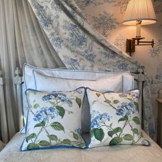 a bed with blue and white pillows on top of it next to a wall mounted lamp