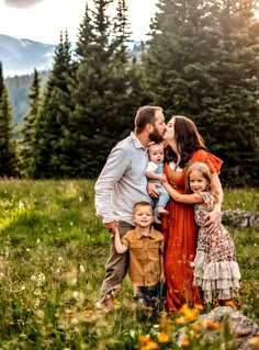 a man and woman kissing their two children in the middle of a field with wildflowers