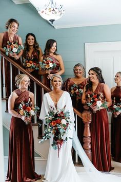 a group of women standing next to each other in front of a stair case holding bouquets