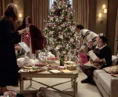 a group of people sitting around a christmas tree in a living room with presents on the table