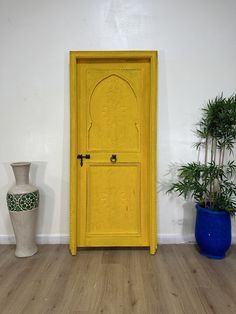 a yellow door is in the corner of a room with two vases and a plant