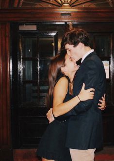 a man and woman embracing each other in front of a doorway with wooden paneling