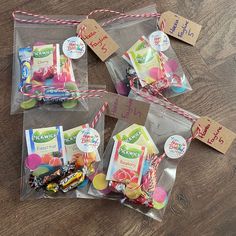 three clear bags filled with candy on top of a wooden table next to some tags