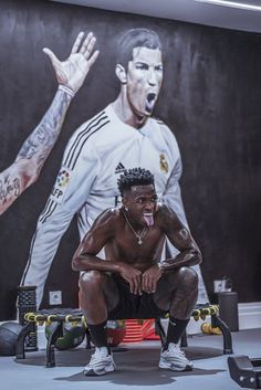 a man squatting down in front of a mural of a soccer player with his mouth open