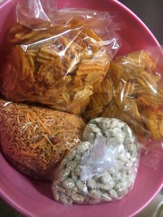 a pink bowl filled with lots of different types of food in plastic wrappers on top of it