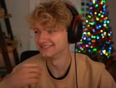 a young man wearing headphones sitting in front of a christmas tree