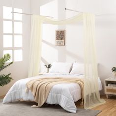 a bed with white sheets and curtains in a bedroom next to a potted plant