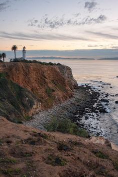 a light house on top of a cliff near the ocean with palm trees in the background