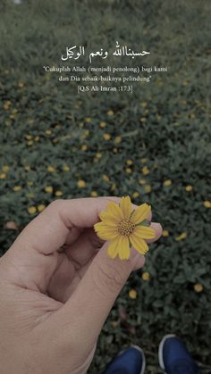 a person holding a small yellow flower in their left hand and looking down at the ground