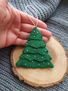 a hand is holding a small green christmas tree ornament on a wood slice