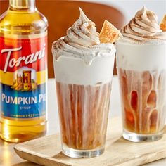 two drinks with whipped cream and pumpkin pie toppings next to a bottle of torani