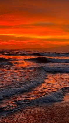 an orange and red sunset over the ocean with waves coming in to shore on a sandy beach