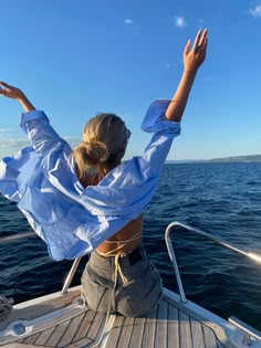 a woman sitting on the back of a boat in the ocean with her arms outstretched