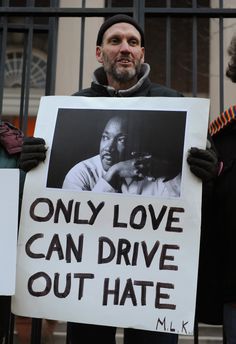 a man holding a sign that says only love can drive out hate