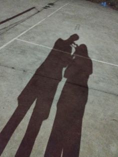 the shadow of two people standing next to each other in front of a tennis court