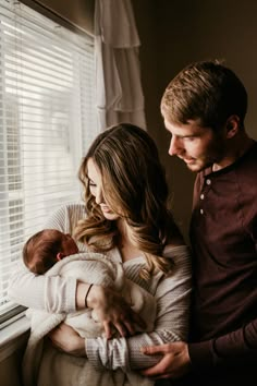 a man and woman holding a baby in front of a window