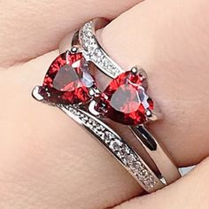 two heart shaped red and white diamond rings on top of each other's fingers