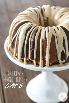 chocolate peanut butter cake with icing on a white cake platter and wooden table